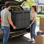Couple carrying large black storage bin out of car trunk during moving day